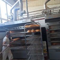 Pracownik piekarni wyjmuje upieczone bochenki chleba z pieca