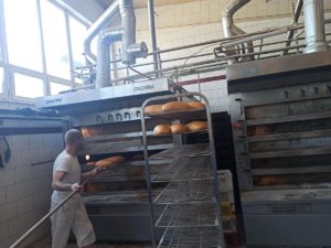 Pracownik piekarni wyjmuje upieczone bochenki chleba z pieca