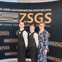 Pani kierownik szkolenia praktycznego z dwiema uczennicami na tle ścianki ZSGS